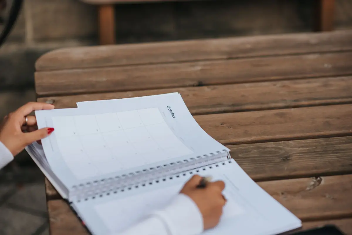 Personne prenant des notes dans un carnet ouvert sur une table en bois