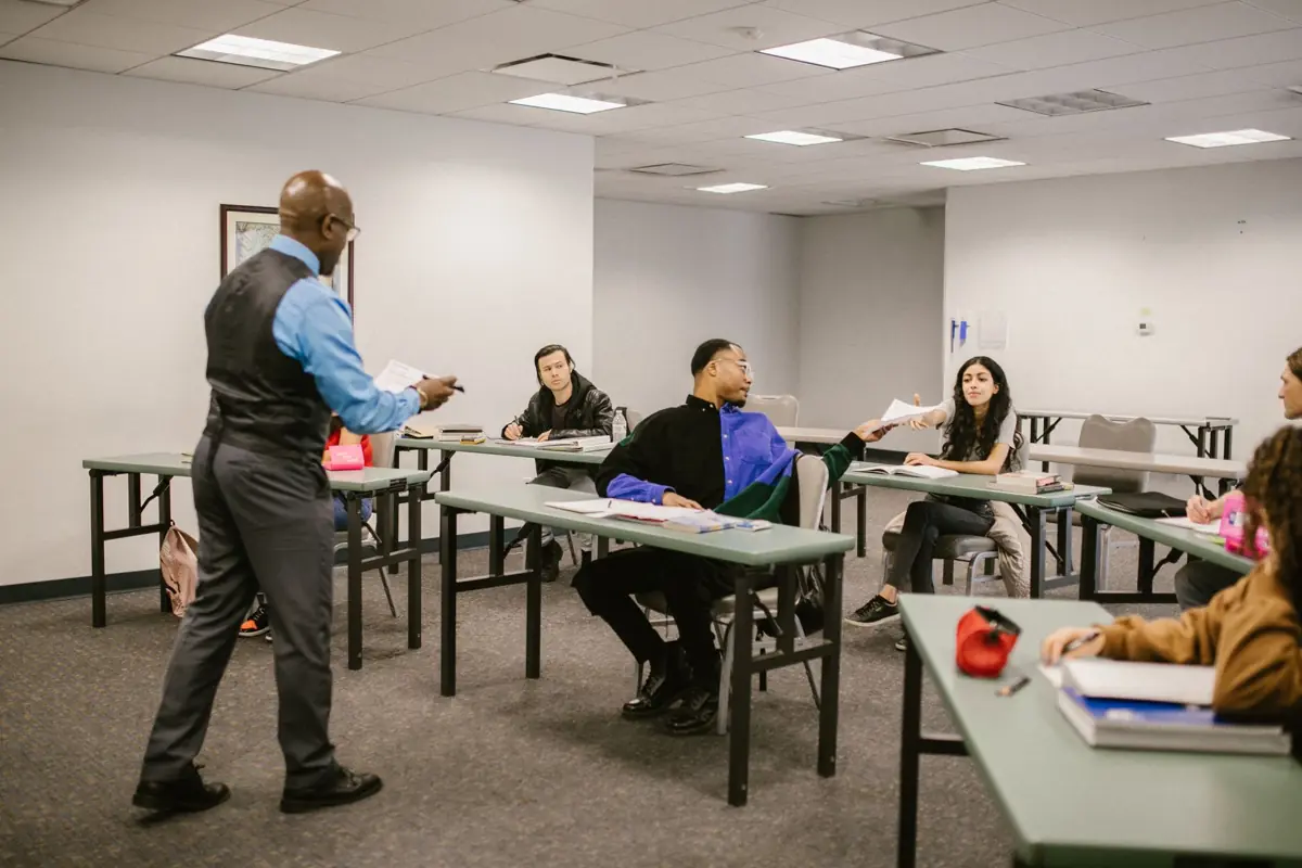 Formateur debout entre les tables d'une salle de formation, face à des participants adultes