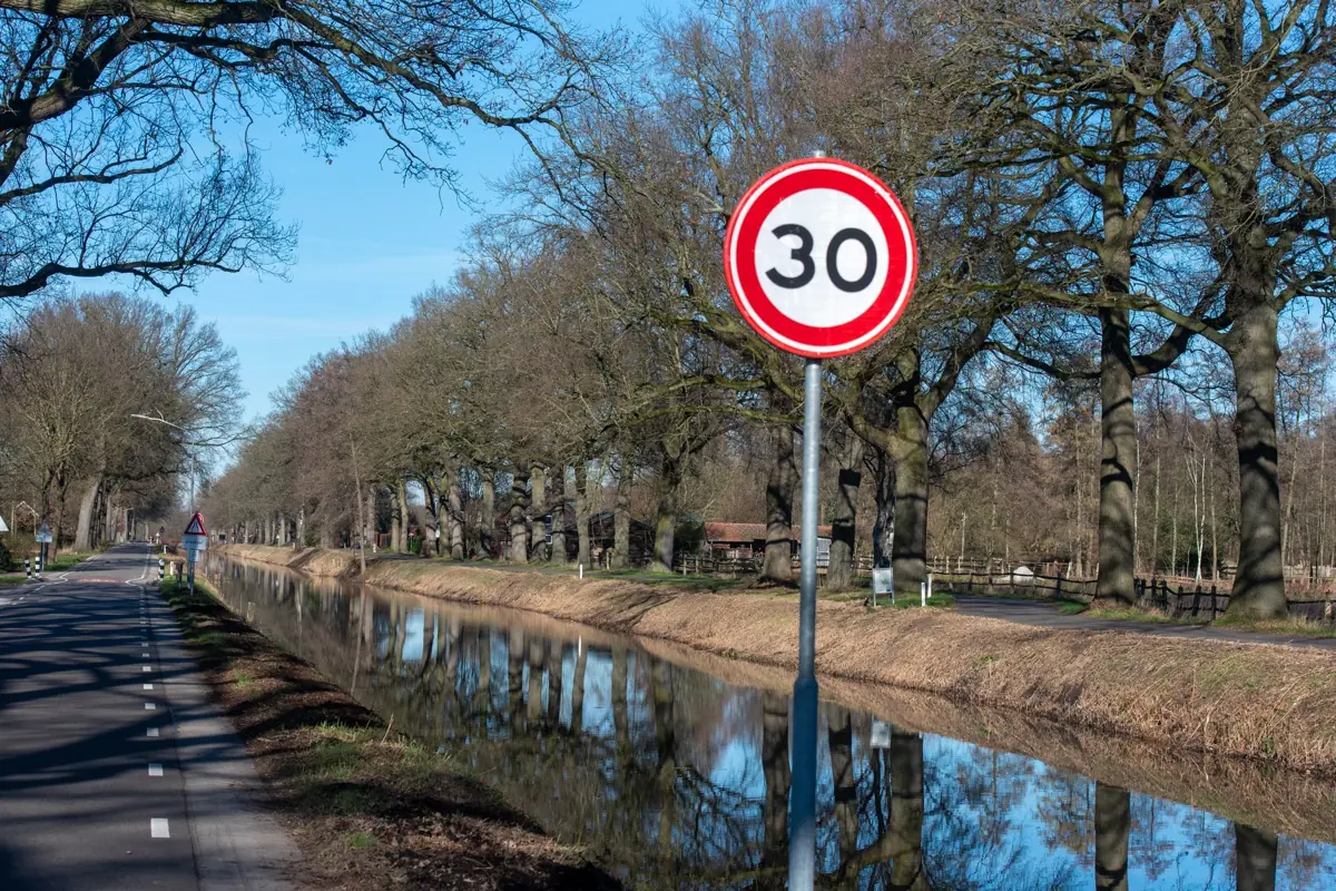 Panneau de limitation de vitesse à 30 km/h au bord d'un canal bordé d'arbres