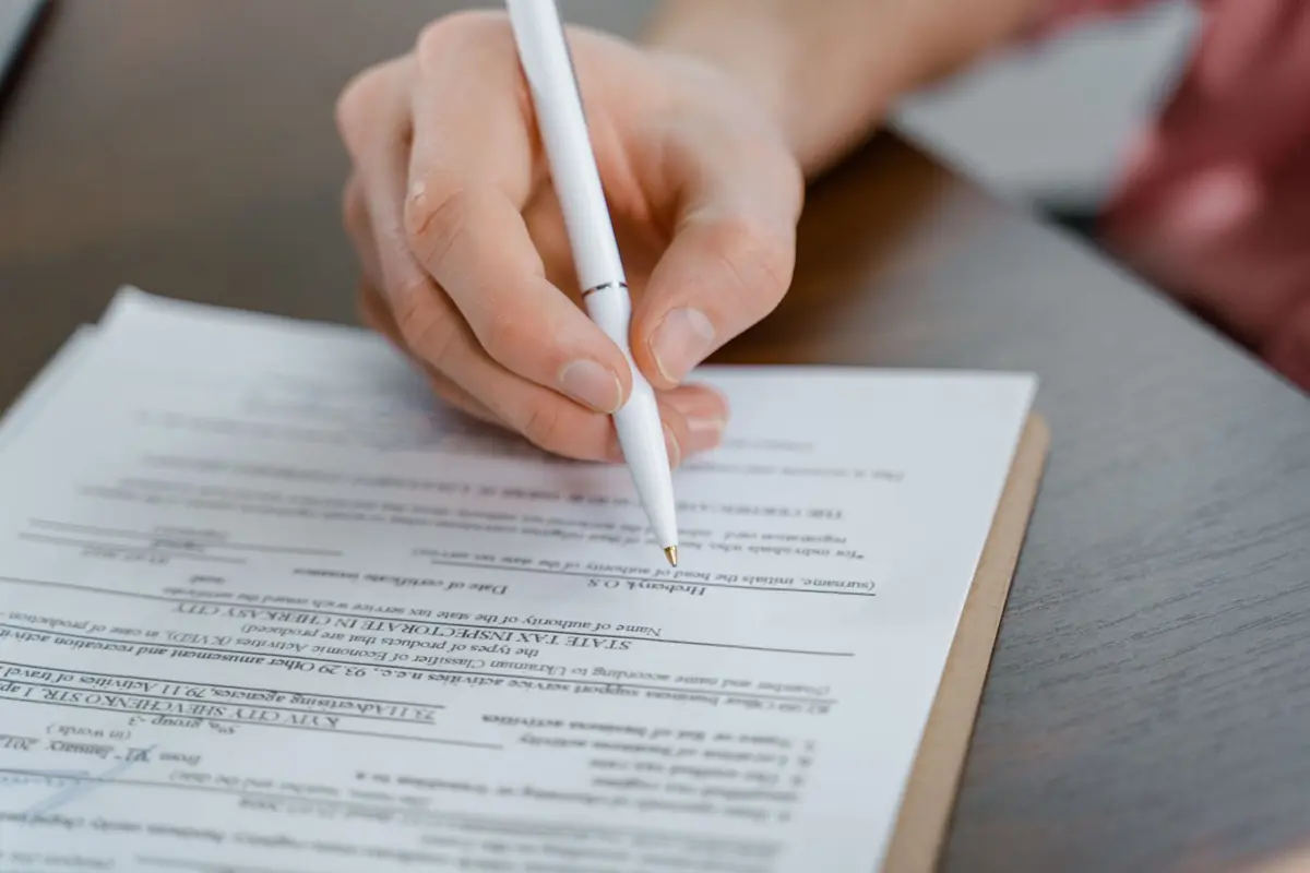Personne remplissant et signant un formulaire posé sur un bureau