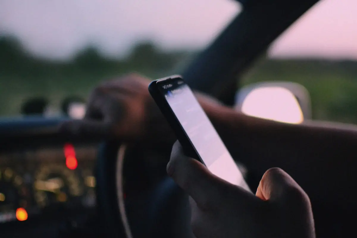 Conducteur tenant un téléphone portable en main au volant, en fin de journée
